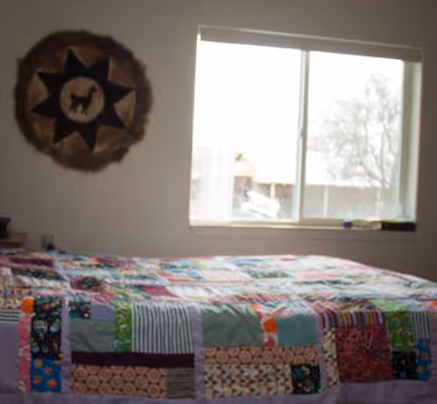 Bedroom with a patchwork quilt on the bed and a decorative wall hanging by the window