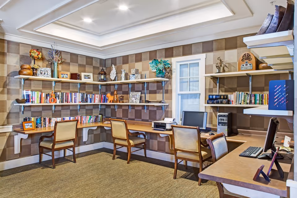 Well-lit communal office/library with built-in desks, chairs, bookshelves and computers against a checkered accent wall.