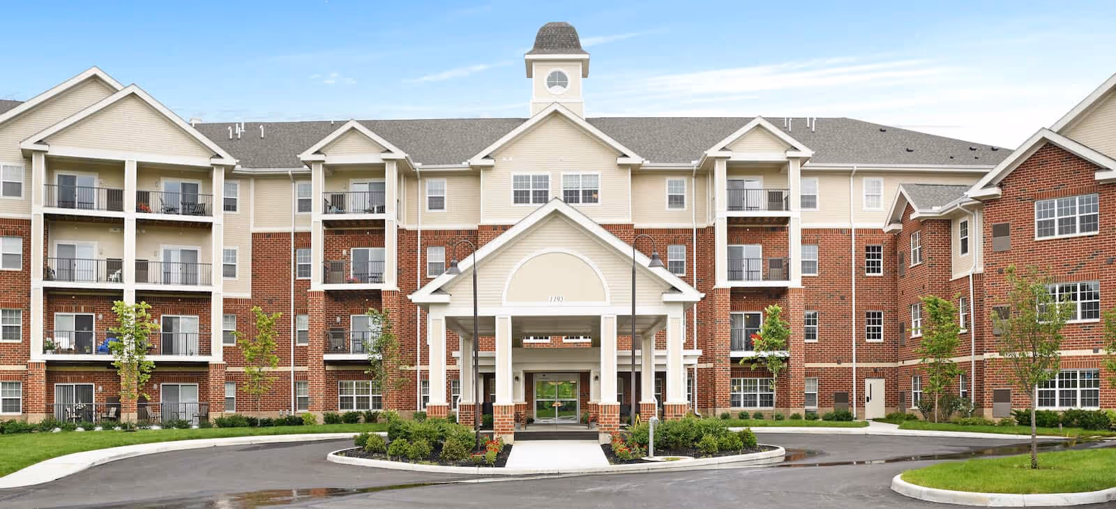 Front exterior of a multi-story brick-and-siding senior living building with a covered porte-cochère entrance and balconies.