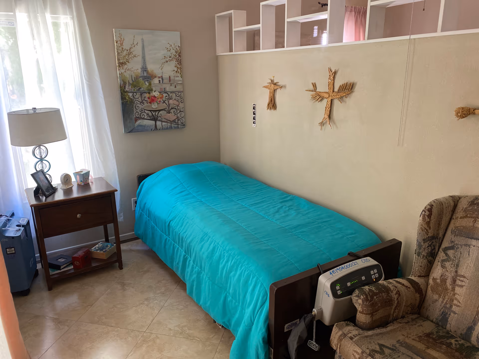 Teal-blanketed bedroom with bed, nightstand, lamp, window, and armchair.