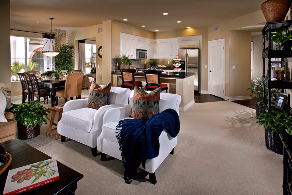 Open-concept living area with two white armchairs facing a kitchen island and a dining table in the background.