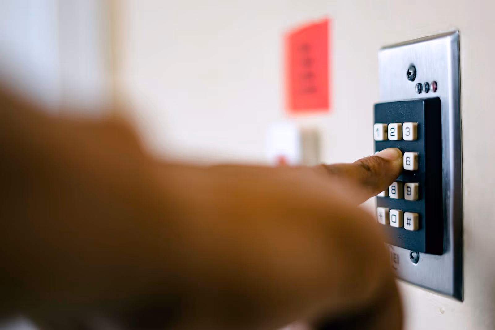Close-up of a person pressing the number 6 on a black keypad mounted on a wall with a metal plate.