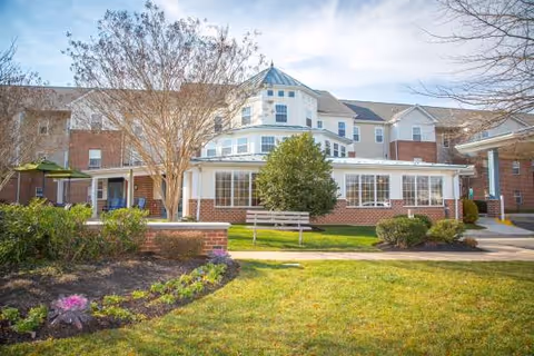 Front exterior view of Arbor Terrace Sudley Manor with landscaped grounds and a bench.