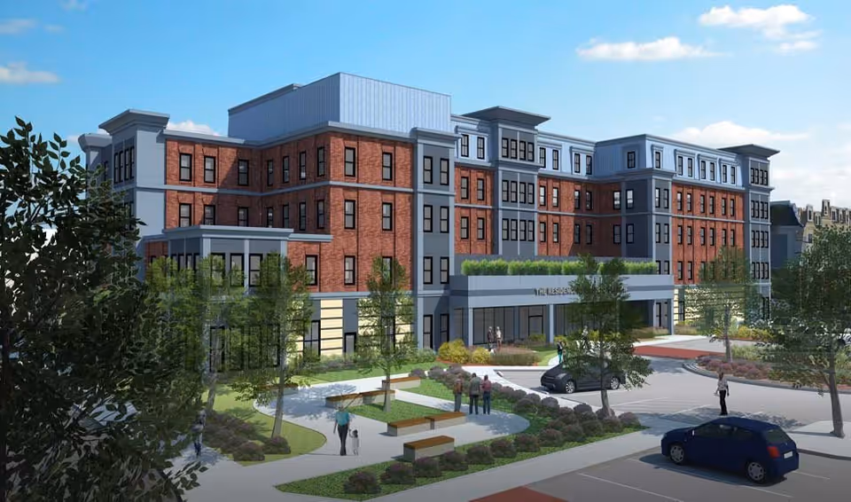 Exterior front rendering of a multi-story brick senior living building with landscaped entrance, benches, and parked cars.