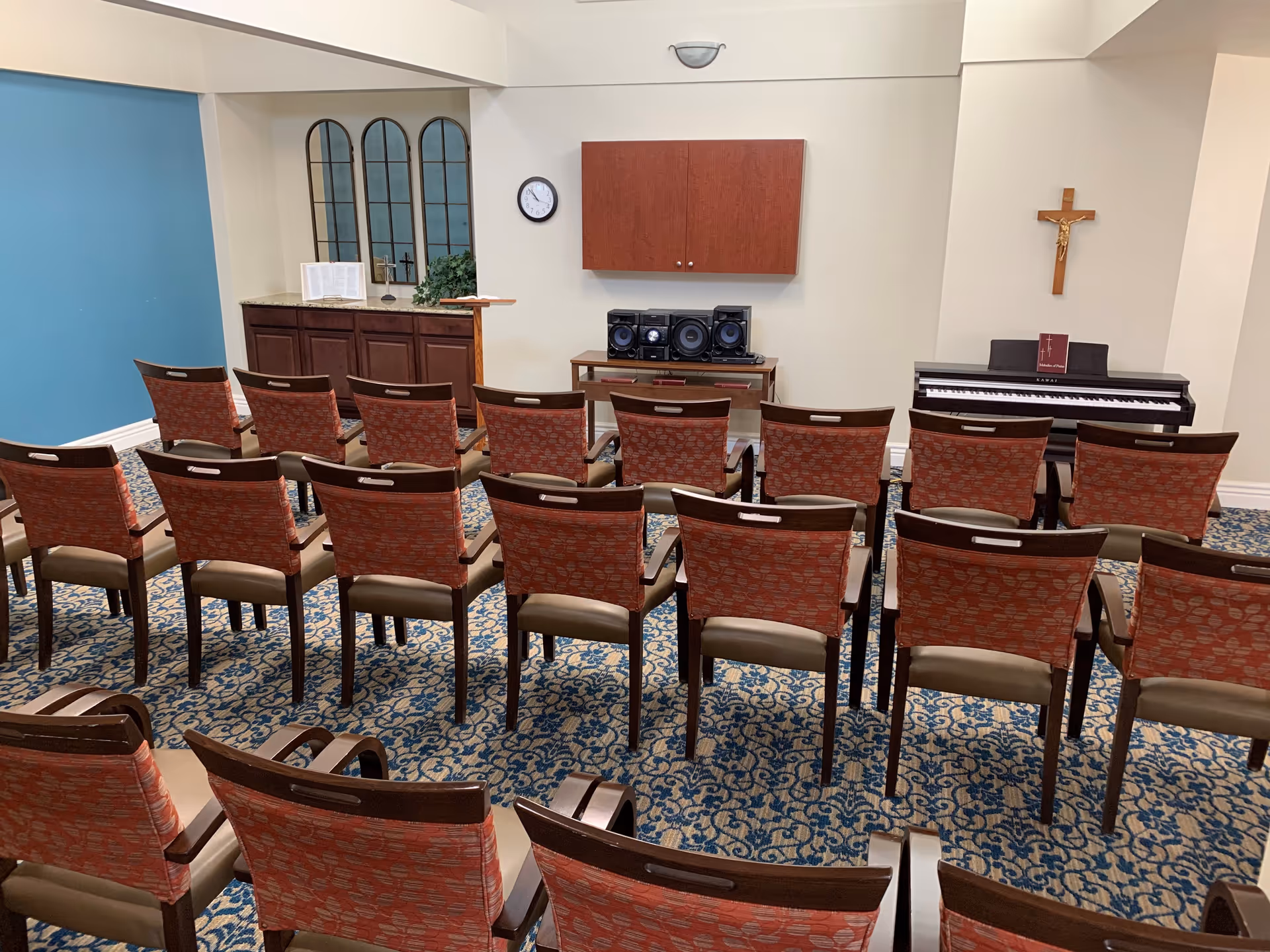 Rows of chairs face a piano and cross on the wall in a small chapel room.