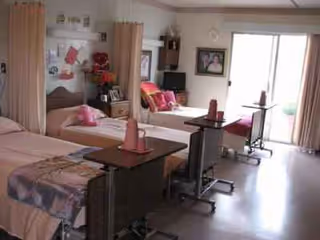 Shared patient room with two beds, curtains, and seating near a window.