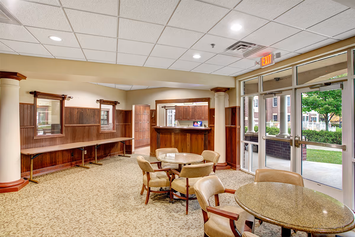 Common area with round tables and chairs, a wooden reception desk, and glass exit doors opening to an outdoor courtyard.