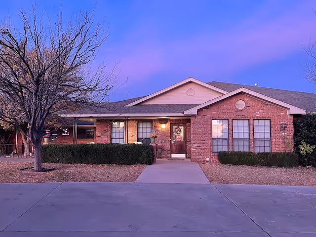Single-story red-brick building with a central entrance, front walkway, trimmed shrubs and leafless trees under a purple evening sky.