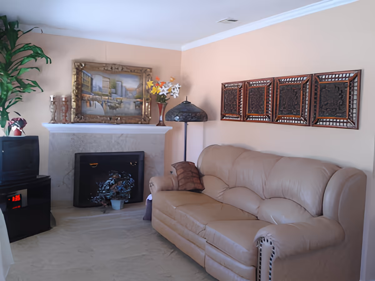 Cozy living room with a beige leather sofa, fireplace topped by a framed painting, TV and decorative wall art.
