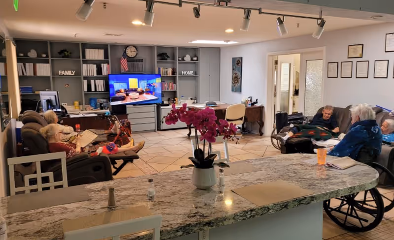 Residents sit in a communal living room watching TV with a kitchen island in foreground