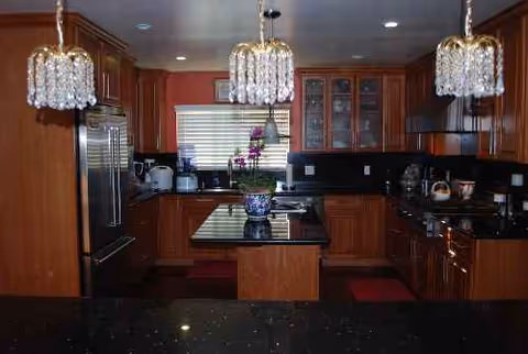 Large kitchen with dark countertops, wooden cabinets, island, and crystal pendant lights.