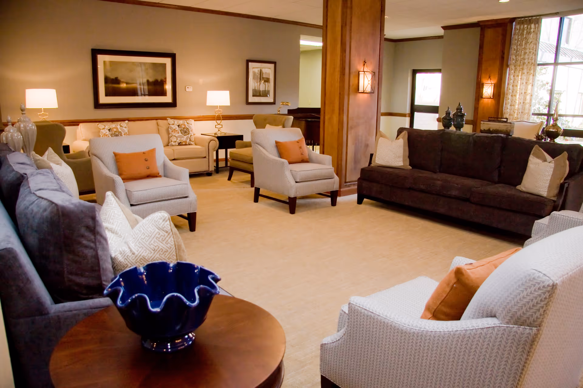 A spacious, well-lit communal living room with sofas, armchairs, lamps, and decorative accents.