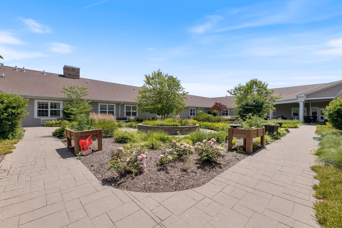 Sunny landscaped courtyard with raised garden beds, walkways, and a surrounding single-story building.