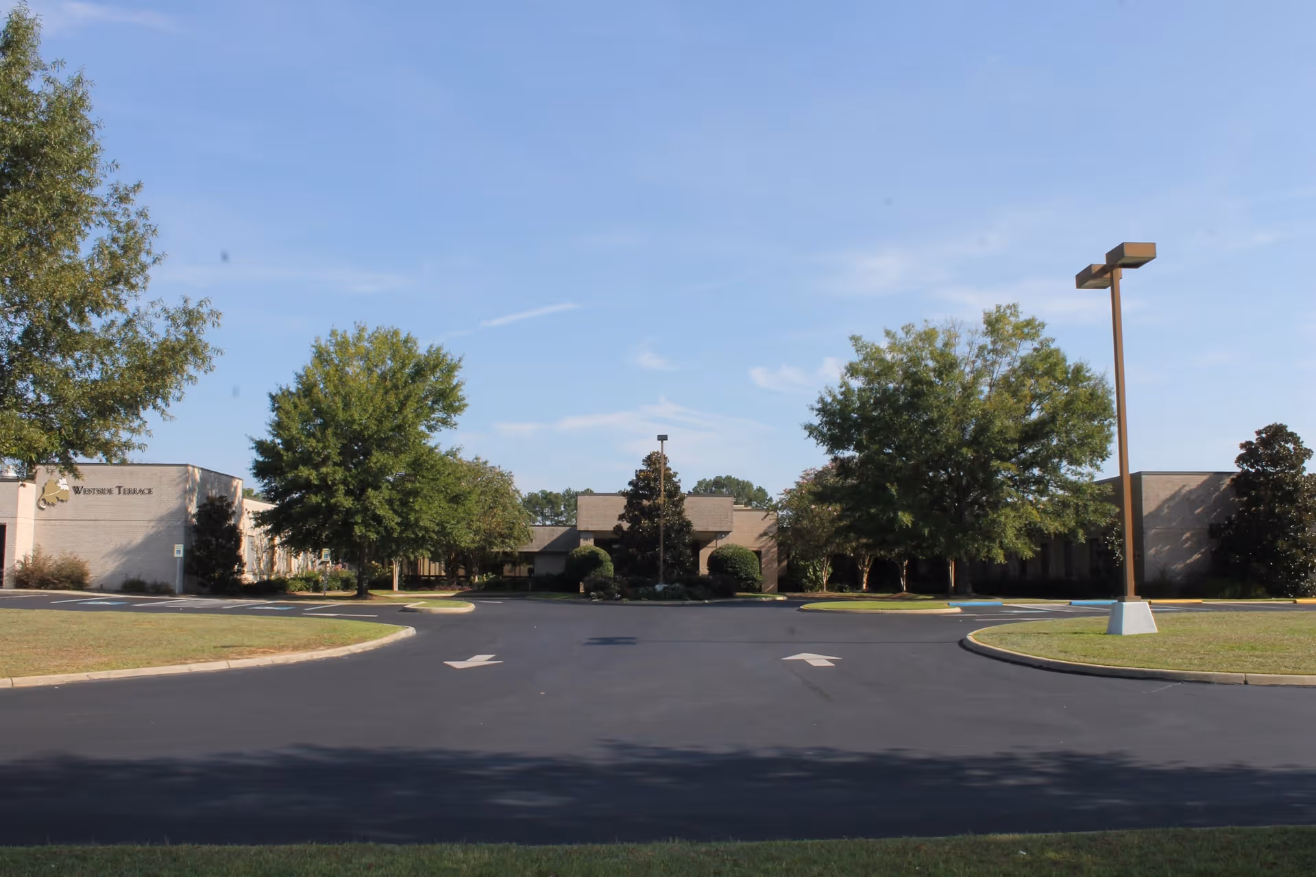Exterior view of Westside Terrace Healthcare building with a paved driveway, green trees, and a clear blue sky.