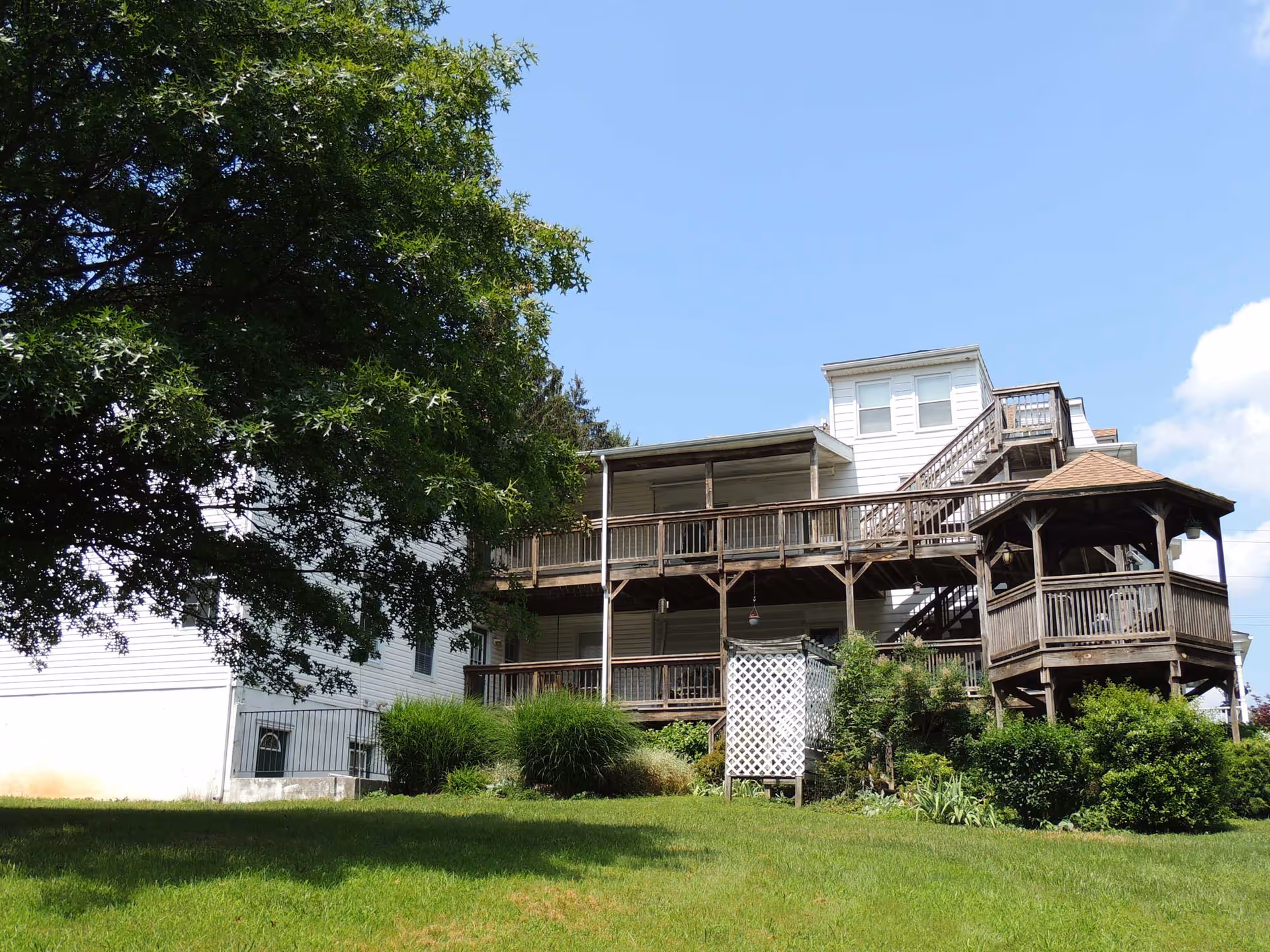 Exterior view of a multi-story assisted living building with wooden balconies and a gazebo, a lawn and large tree in the foreground.