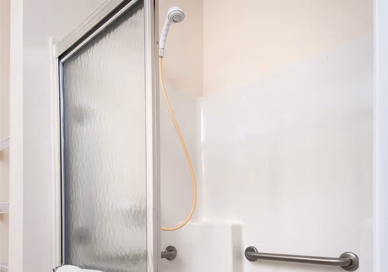 Shower stall with a frosted sliding door, a handheld showerhead with a yellow hose, and a grab bar.