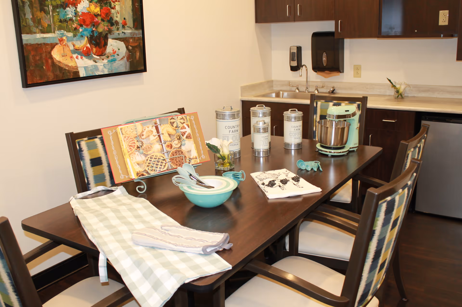 A dining table in a kitchenette area set with bowls, utensils, a stand mixer and decorative canisters.