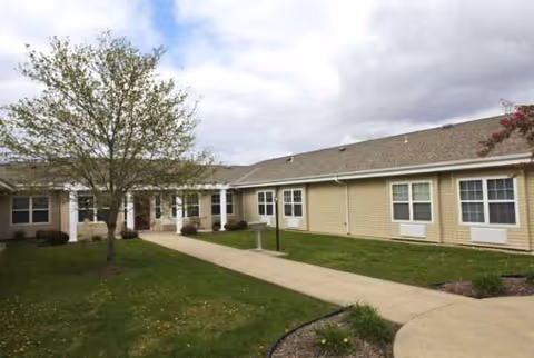 Single-story senior living facility exterior with a central entrance and surrounding green lawn.