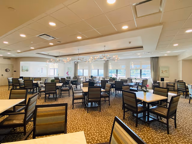 Spacious dining room with multiple tables and chairs, modern chandeliers, and large windows letting in natural light.