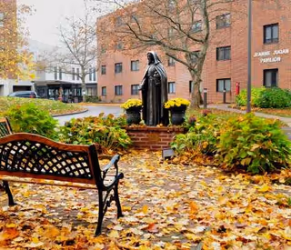 Statue and bench in an autumn courtyard with fallen leaves at Jeanne Jugan Residence.