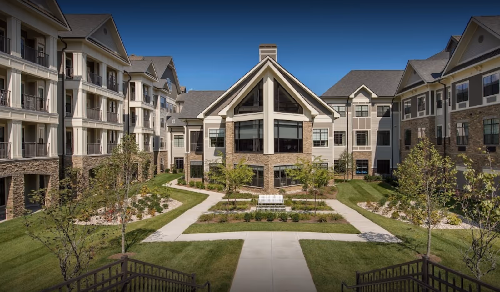 Landscaped courtyard with walkways and a bench surrounded by a multi-story senior living building.