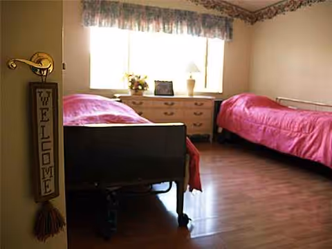 Two single beds with pink covers overlook a dresser beneath a window in a bedroom.
