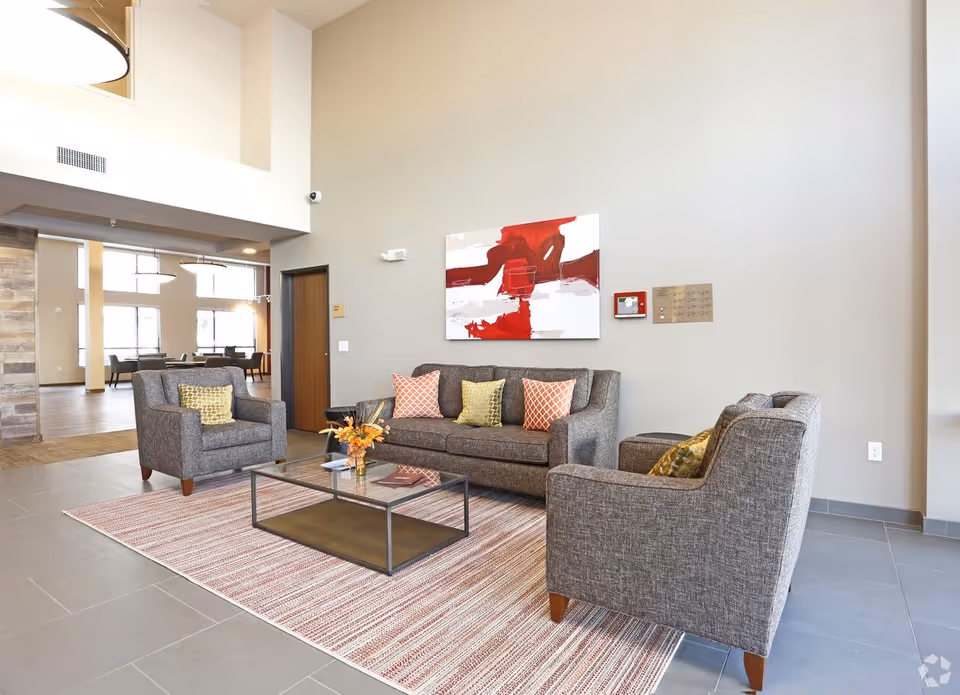 Modern lobby seating area with gray sofas and armchairs around a glass coffee table and abstract red wall art.