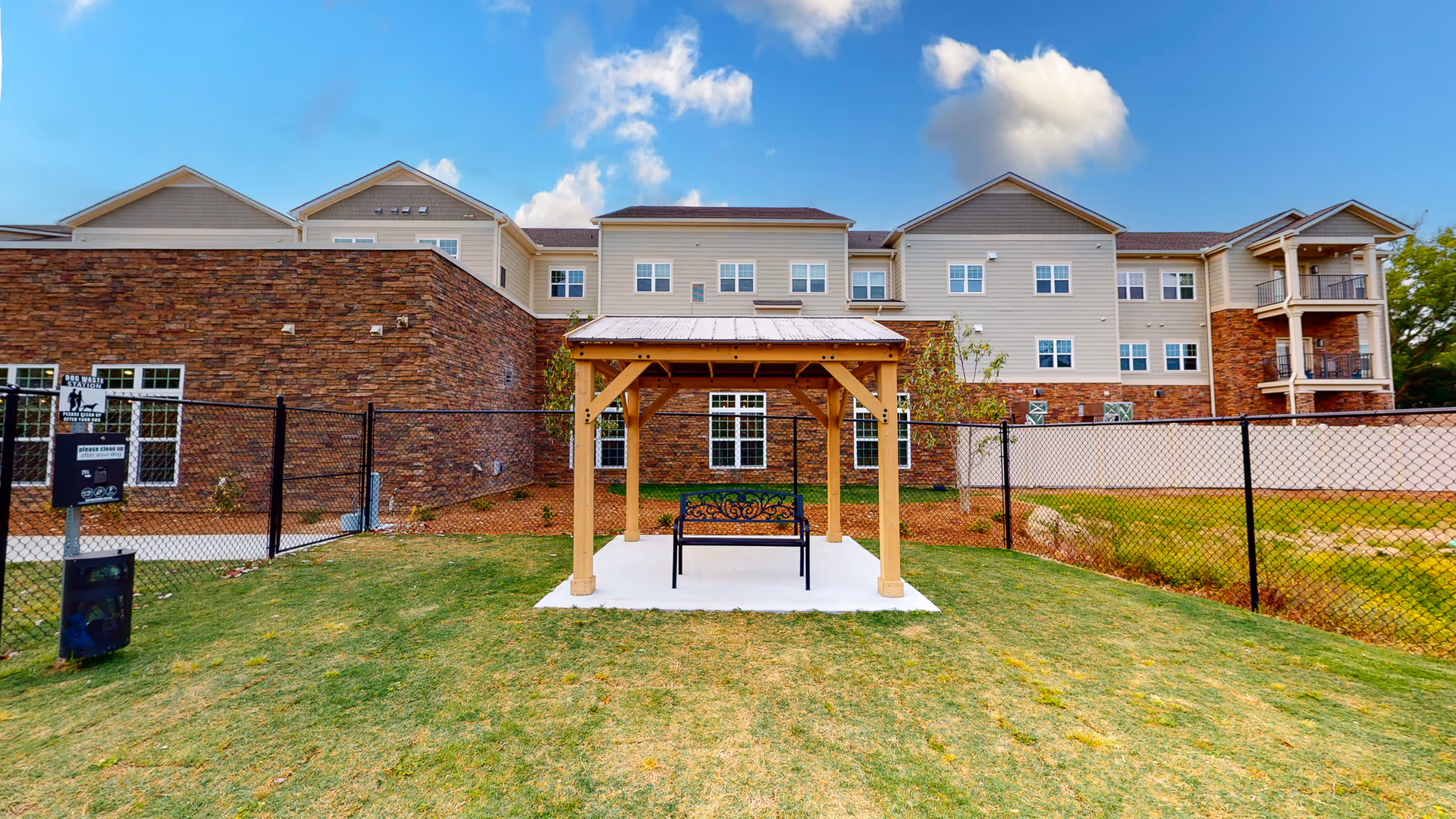 View of the exterior of Legacy Reserve at Fairview Park, featuring a wooden gazebo with a bench in the foreground and a stone and siding building in the background.