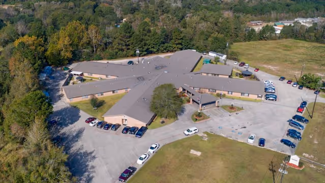 Aerial view of Southland Rehabilitation And Healthcare Center, a single-story building with a cross-shaped layout surrounded by trees and parking lots with several cars parked.