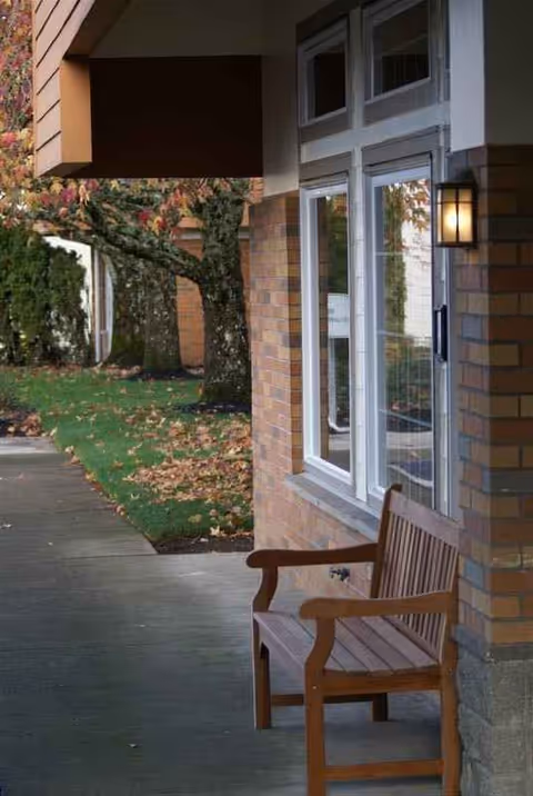 Brick exterior of a senior living facility with a wooden bench outside.