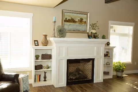 Cozy living room with a white fireplace mantel flanked by built-in shelves, decorative items, and windows.