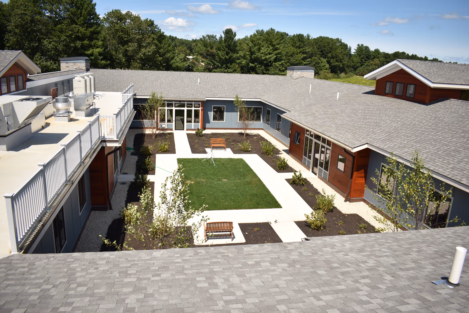A central landscaped courtyard with a grassy square, walkways and benches surrounded by single-story building wings and rooftops.