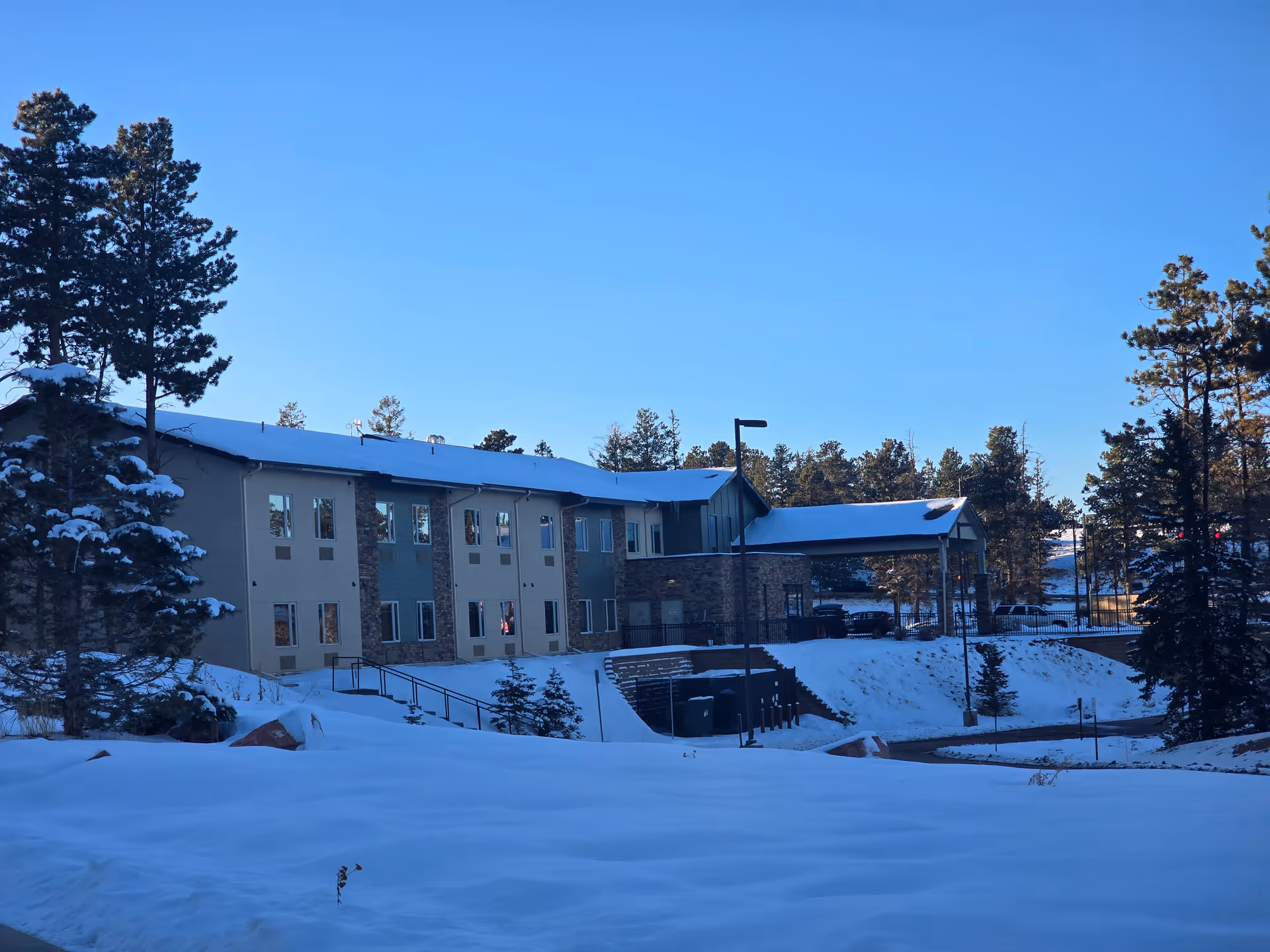 Exterior view of a two-story senior living facility building named Forest Ridge Senior Living, surrounded by snow-covered ground and trees under a clear blue sky.