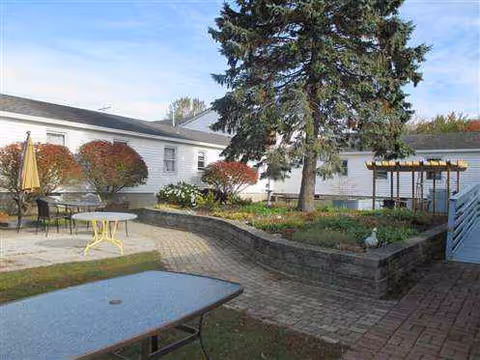 Outdoor courtyard with brick paths, seating, stone garden beds, a large tree, and a pergola