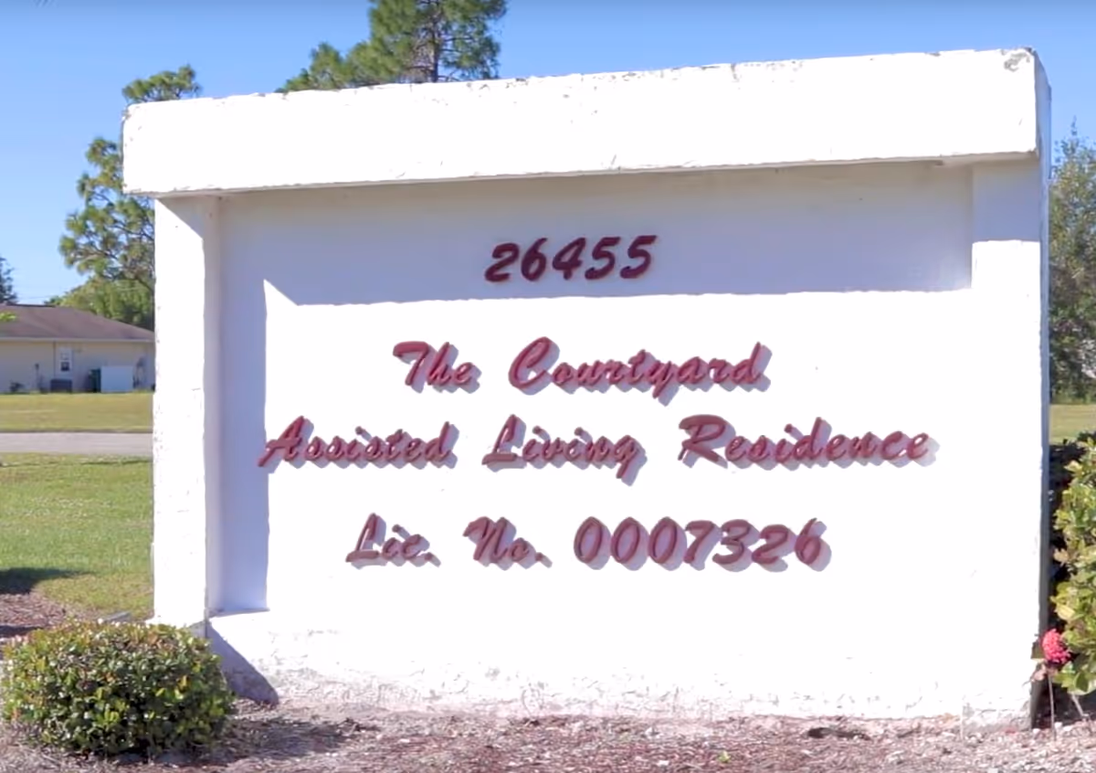 White roadside sign on a grassy lawn showing '26455' and 'The Courtyard Assisted Living Residence'.