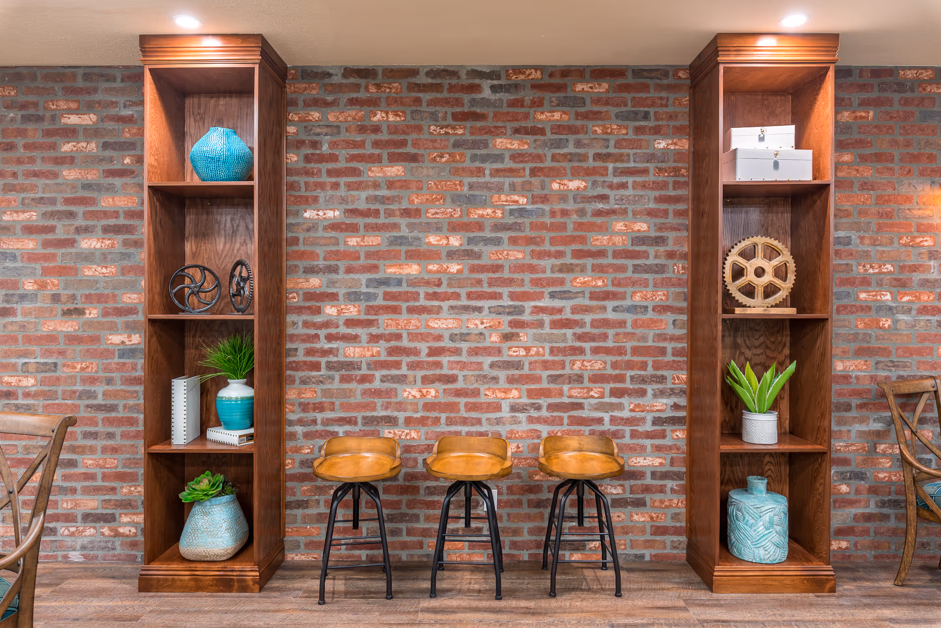 Interior communal seating area with an exposed brick wall, two tall wooden bookcases and three leather bar stools.