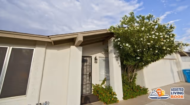 Front entrance of a single-story house with a metal security door, a flowering tree by the doorway, and an attached garage.