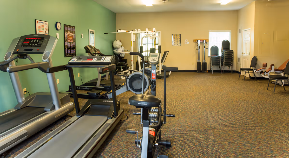 An interior exercise room with treadmills, stationary bikes, and weight equipment in a senior living facility.