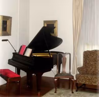 A grand piano with bench and chairs in a well-lit living room.