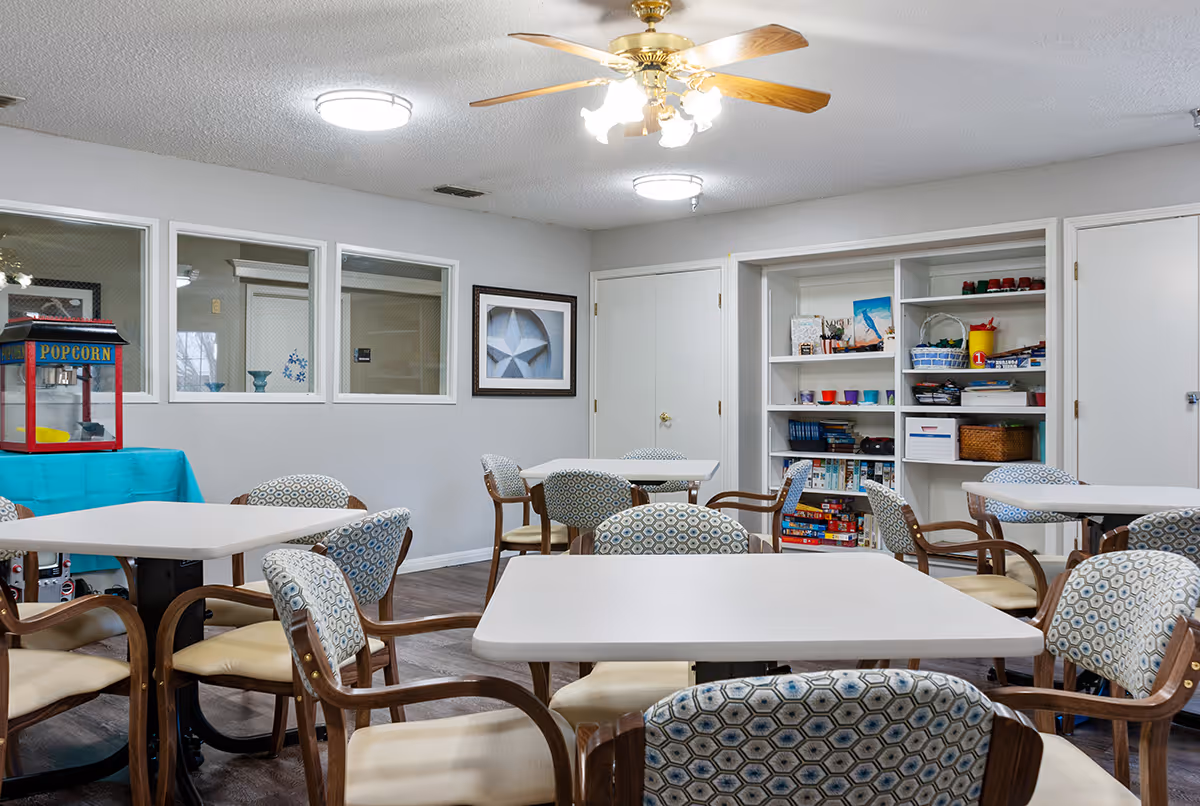 Activity/dining room with multiple tables and patterned chairs, shelves of games and a popcorn machine.
