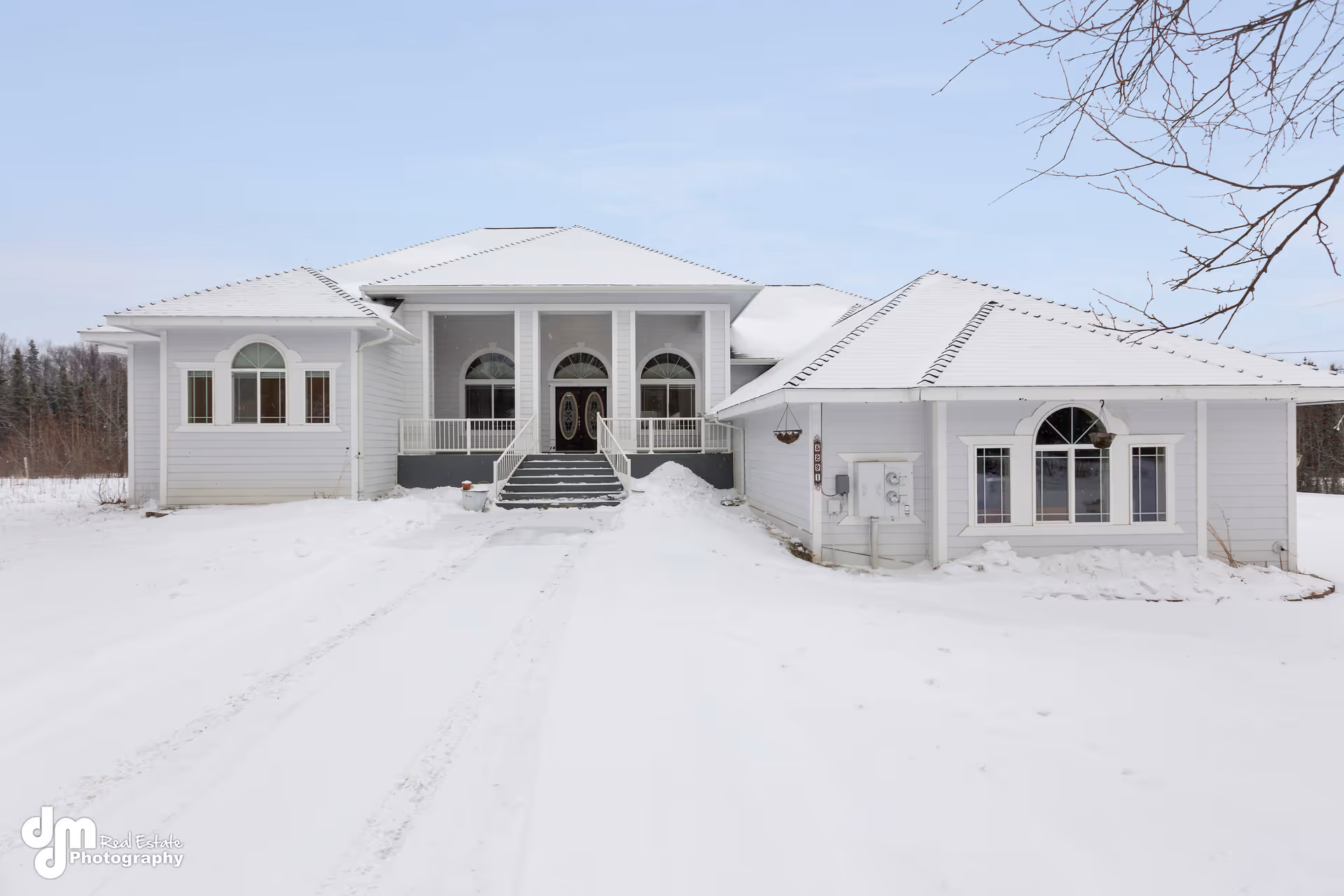 Front exterior of a snow-covered white house with central steps and arched windows.