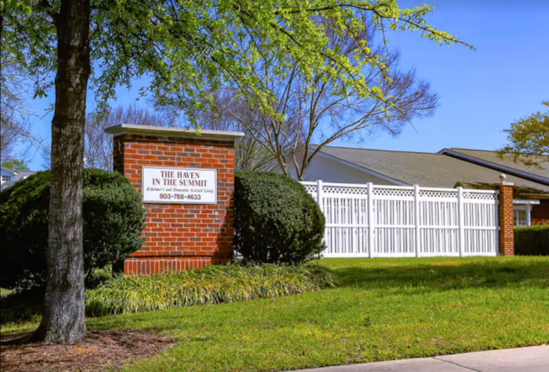 Brick entrance sign reading 'The Haven in the Summit' beside a white fence and landscaped lawn in front of the facility.