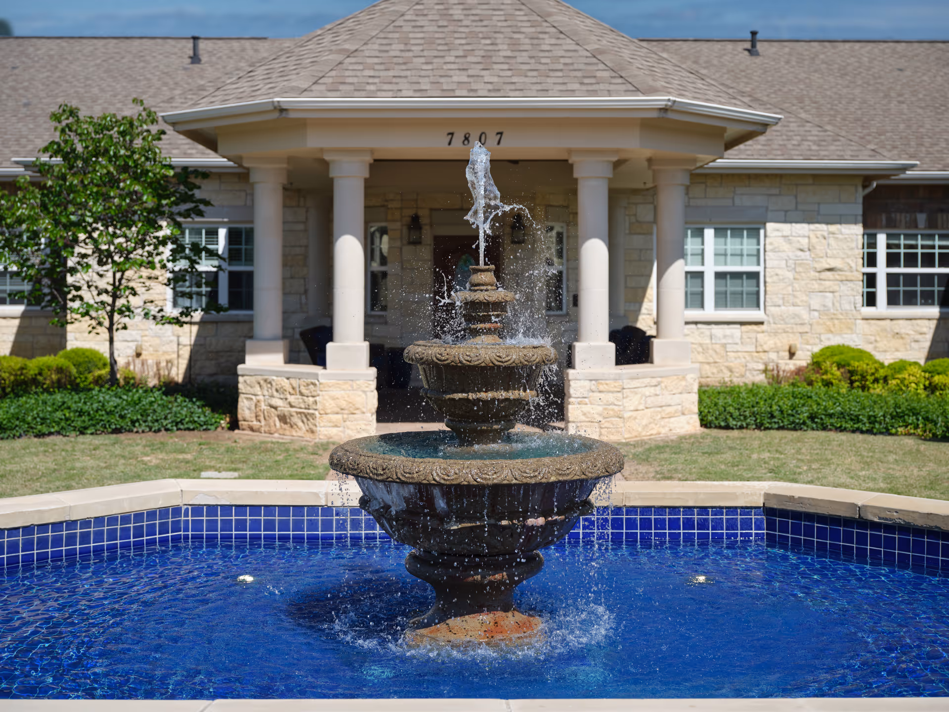 Exterior view of a memory care facility with a central fountain at the entrance.