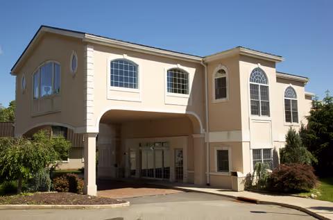 A beige two-story senior living facility with arched entrance and large windows.