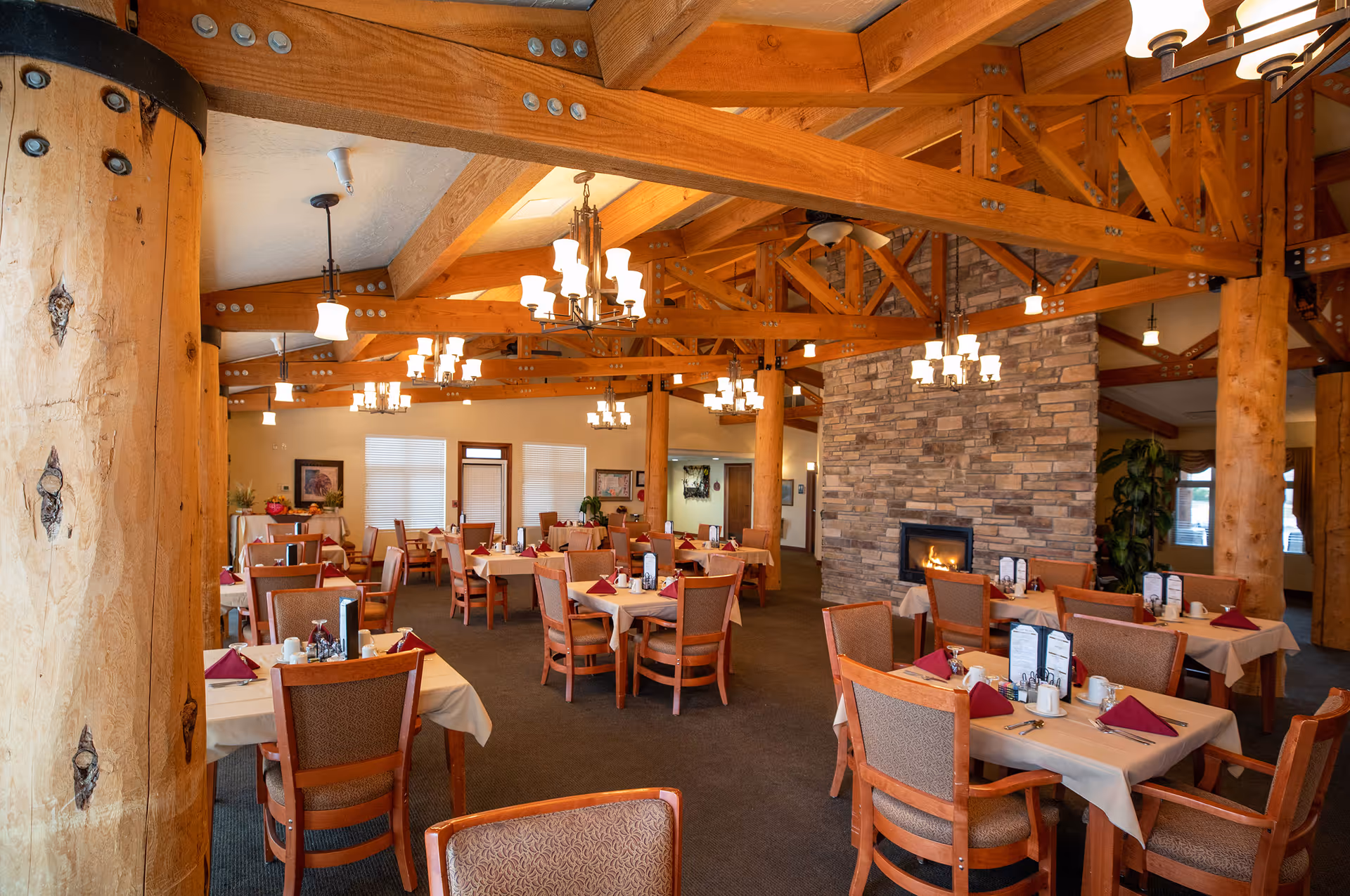 Spacious dining room with exposed wooden beams, multiple set tables and chairs, and a stone fireplace.