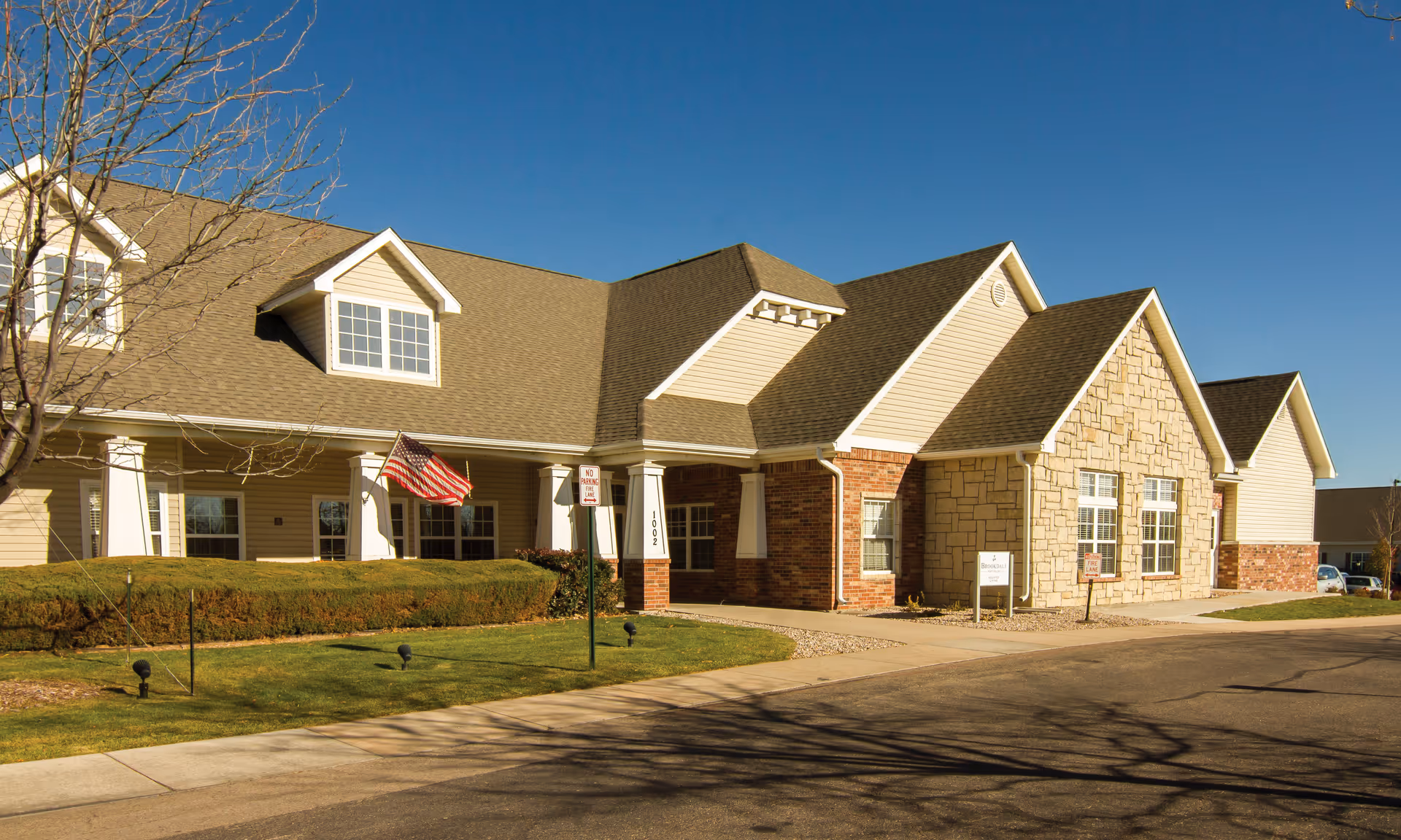 Senior living facility exterior with stone accents, gabled roof, and manicured lawn.