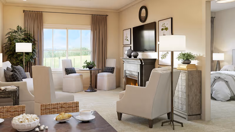 A cozy living room with beige walls and carpet, featuring a fireplace with a TV mounted above it. There are several upholstered chairs and a sofa with cushions arranged around a small round table near a large window with curtains. A floor lamp and a side table with books and a plant are also visible. In the foreground, a dining table with a bowl of popcorn, a croissant on a plate, and a cup of coffee is partially visible. A bedroom with a bed and bedside lamp can be seen through an open doorway.