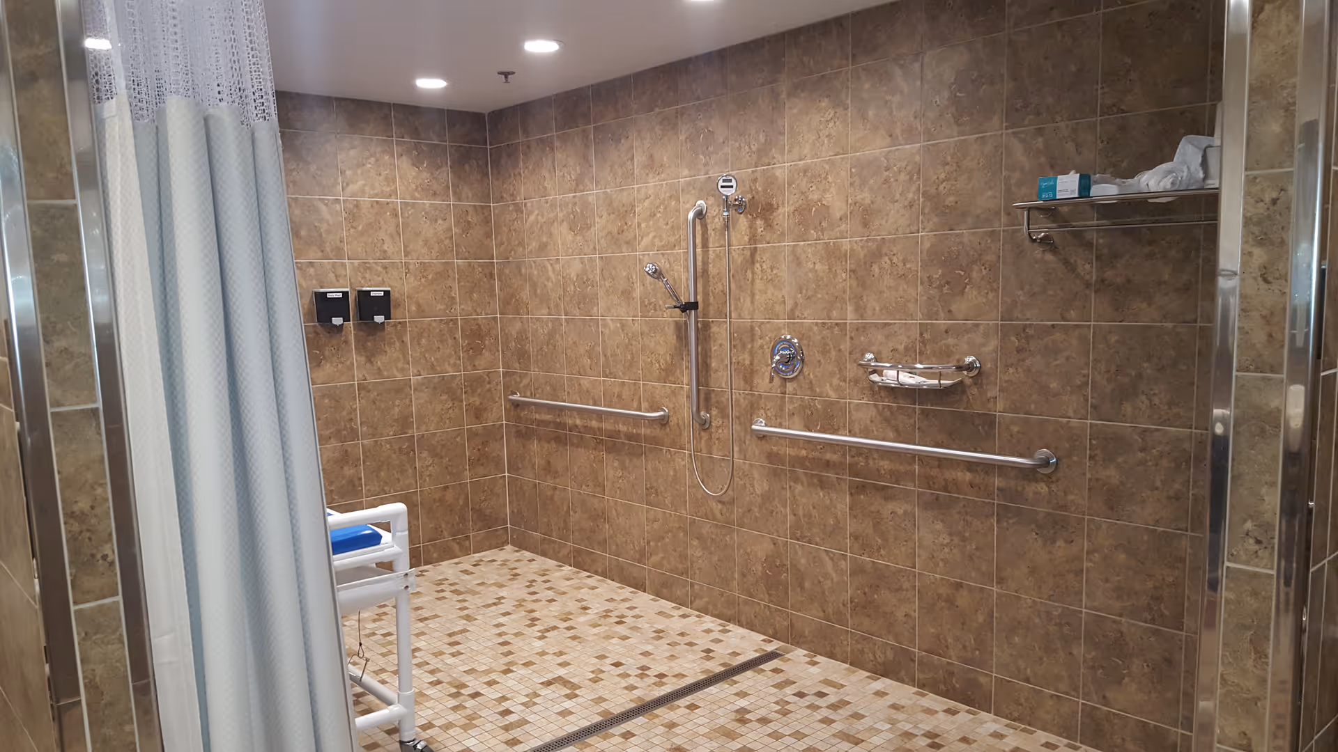 Accessible tiled shower room with grab bars, handheld shower, shower chair and a privacy curtain.