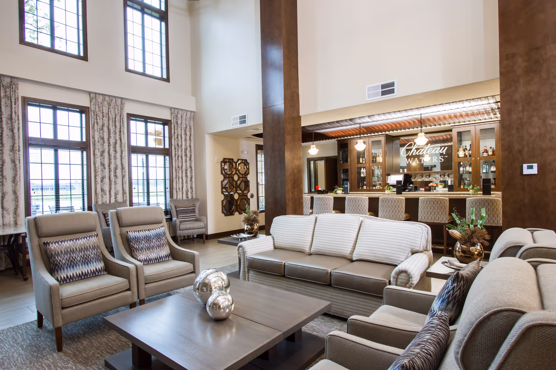 Bright communal lounge with upholstered sofas and armchairs facing a coffee table and a bar area labeled 'Chateau Waters'.