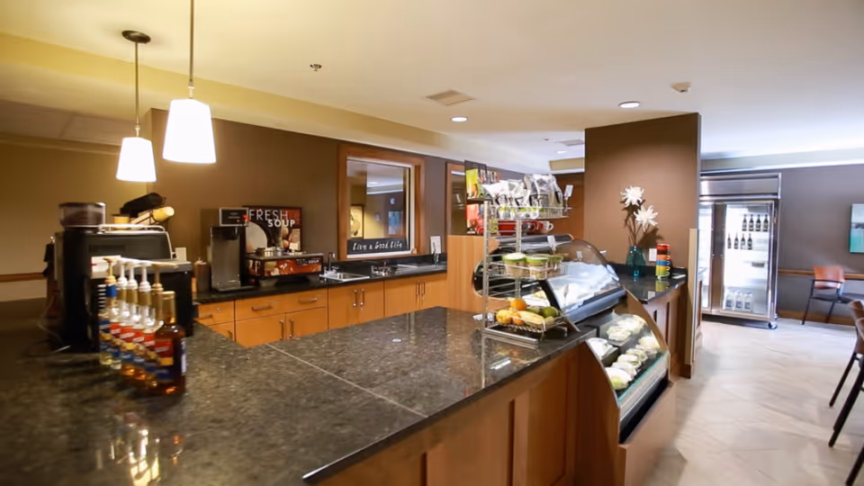 Interior cafe-style dining area with a granite service counter, pastry display case, coffee station and refrigerated drinks.